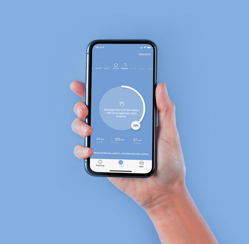 Eine Hand hält ein Smartphone, das eine App mit einem Fortschrittsdiagramm zeigt. Die Anzeige informiert darüber, dass 39 % des täglichen Ziels erreicht wurden. Der Hintergrund ist in einem hellblauen Farbton gehalten.
