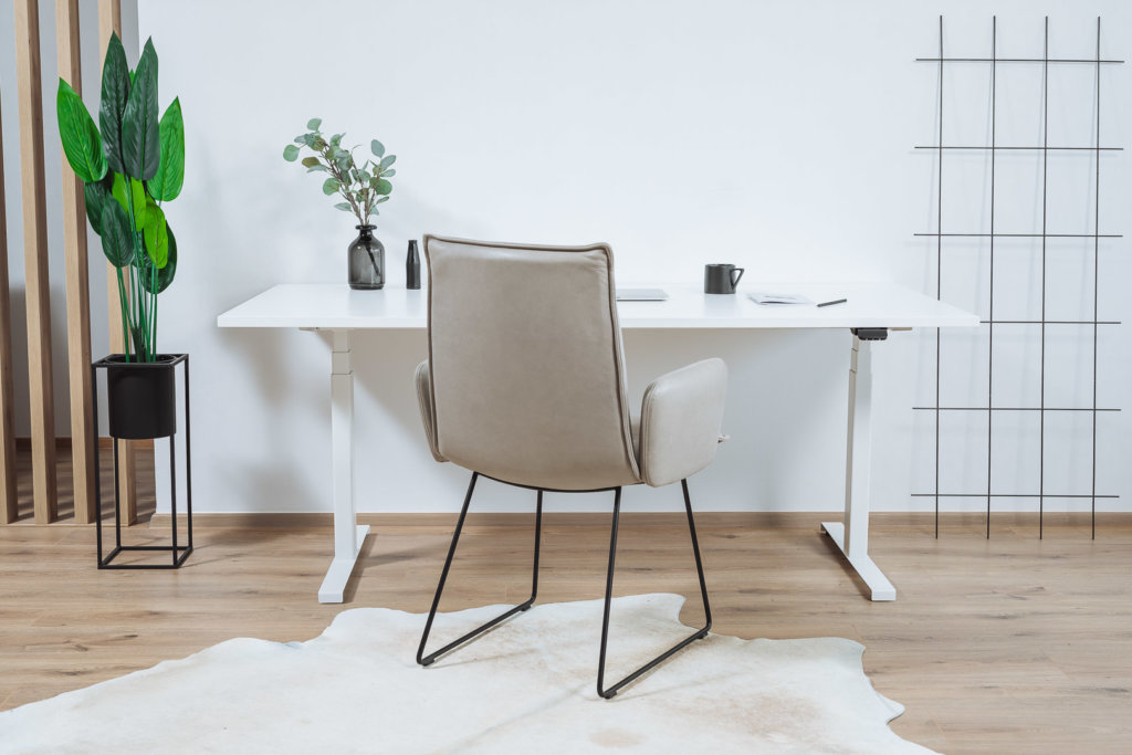 Elektrisch höhenverstellbarer Schreibtisch in weiß in einem Home Office mit einem Sessel davor.