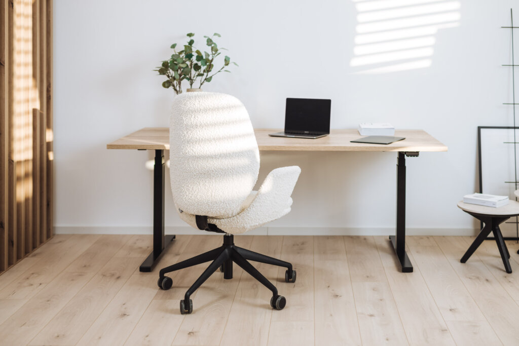 Ein höhenverstellbarer Schreibtisch mit schwarzem Gestell und heller Holzplatte in einem hellen Raum. Ergänzt durch einen bequemen Bürostuhl, Pflanzen und minimalistisches Dekor.